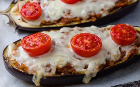 Deux aubergines farcies, garnies de tomates et de fromage fondu, prêtes à être dégustées.