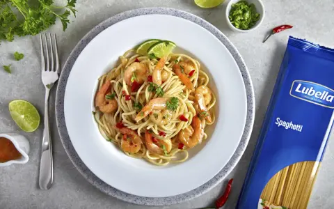 Pyszny makaron z krewetkami na winie, udekorowany limonką i natką pietruszki. Obok opakowanie makaronu spaghetti Lubella.