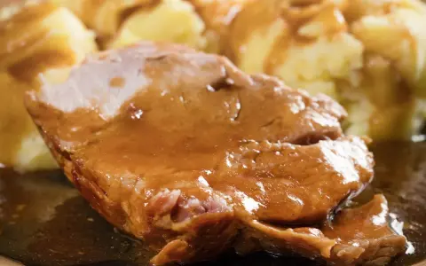 Mięciutka karkówka w sosie, podana z purée ziemniaczanym. Danie wygląda apetycznie i soczyście.