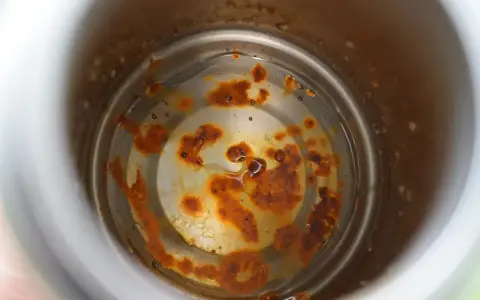 Intoxication eau gourde : intérieur rouillé d'une gourde, avec des dépôts orangés et de l'eau trouble.