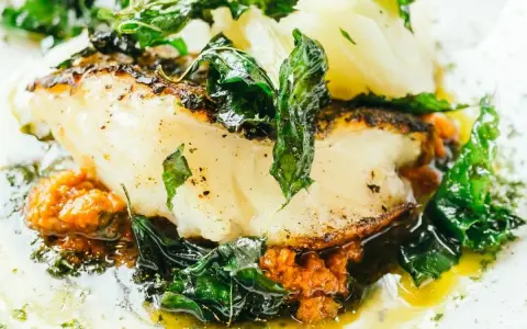 Delicioso bacalao al pil pil, con su piel dorada, acompañado de verduras frescas y una salsa vibrante.