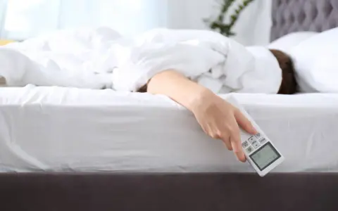 Mano che tiene il telecomando del condizionatore, con la persona che cerca il **significato** di un **sonno** confortevole.