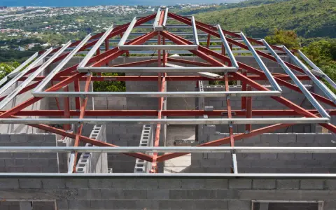 Structure métallique d'une maison en construction, avec des poutres rouges et grises. Un inconvénient potentiel de ce type de maison est la nécessité d'une isolation thermique soignée.