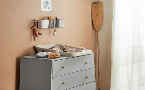 Eine Wickelkommode organisieren: Spielzeug, Handtücher und Pflegeutensilien sind ordentlich verstaut. Ein Holzpaddel lehnt an der Wand.