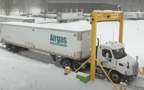Ciężarówka z naczepą Airgas pod żółtą bramownicą w śnieżny dzień.
