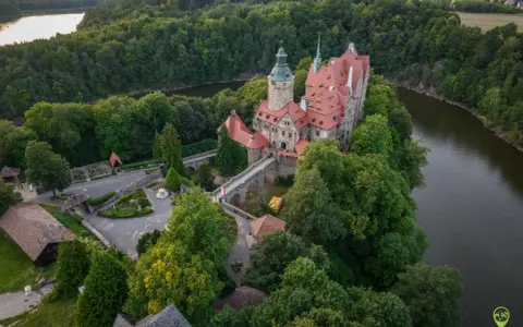 Zamek Czocha, malowniczo położony na skalistym cyplu nad rzeką, otoczony bujną zielenią.