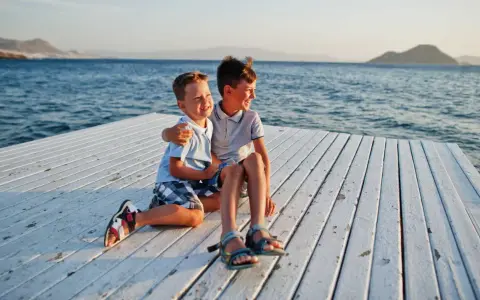 Dos niños sonríen sentados en un muelle blanco. ¡Ideas para que hacer en Murcia con niños!