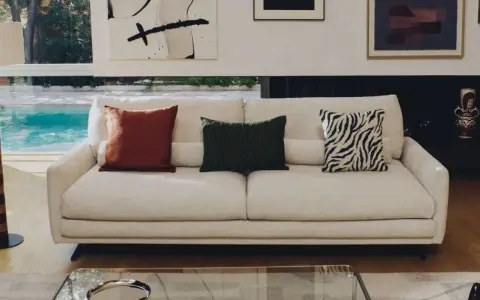 Sofá blanco con cojines decorativos: uno rojo, uno verde con textura y otro con estampado de cebra.