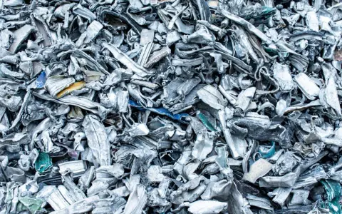 Góra poskręcanego, poszarpanego złomu metalowego, gotowego do recyklingu metalu. Widać fragmenty niebieskiego i żółtego plastiku.
