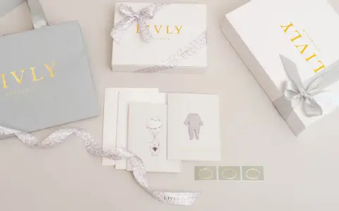 En nyfödd present box från Livly Stockholm med en grå påse, vita boxar med guldig text och leopardmönstrat band. Kort med illustrationer av en elefant och en babybody.
