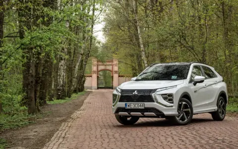 Biały Mitsubishi Eclipse Cross na tle bramy i drzew. Wiele pozytywnych mitsubishi eclipse cross opinie potwierdza jego wszechstronność.