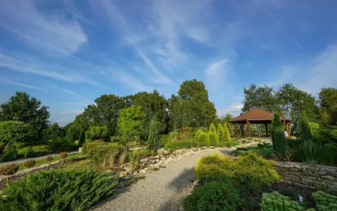 Malownicze ogrody botaniczne na Śląsku z altaną i kamiennymi ścieżkami, otoczone bujną zielenią pod błękitnym niebem.