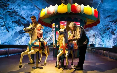 Familj njuter av en karusell i en grottliknande miljö på Stockholm Toy Museum.