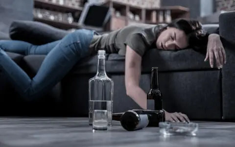 Kobieta leży nieprzytomna na kanapie, obok butelki i szklanka. Czy alkoholik może pić kontrolowanie? To pytanie pozostaje bez odpowiedzi.