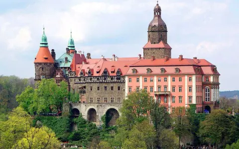 Malownicze zamki i pałace wokół Wrocławia, jak ten imponujący kompleks z wieżami i czerwonymi dachami, zachwycają architekturą i otoczeniem.