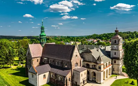 Wąchock atrakcje: Opactwo Cystersów z zieloną wieżą i wieżą zegarową na tle błękitnego nieba z chmurami.