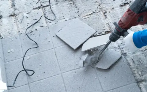 Skuwanie płytek młotem udarowym. Widać fragmenty rozbijanej podłogi i kabel zasilający.