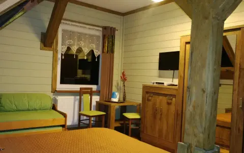 Przytulny pokój w schronisku Śnieżne Kotły. Zielona kanapa, drewniane meble i widok z okna.