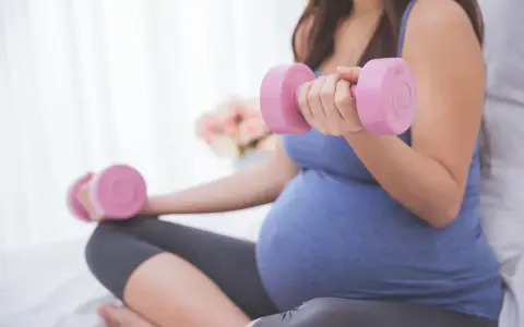 Ciężarna kobieta wykonuje ćwiczenia z hantlami, przygotowując się do porodu.