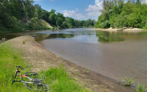 Rower leży na trawie nad rzeką, otoczoną zielenią. To malowniczy zakątek, prawdziwa szwajcaria podlaska.