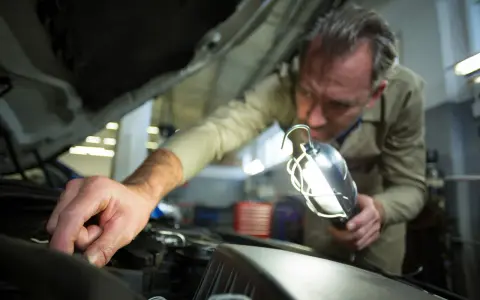 Meccanico controlla il motore con una lampada per capire se la batteria auto è da cambiare.
