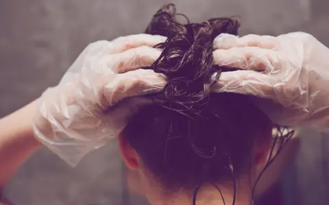 Hände mit Handschuhen tragen Olaplex Nr. 3 auf nasses, dunkles Haar auf.