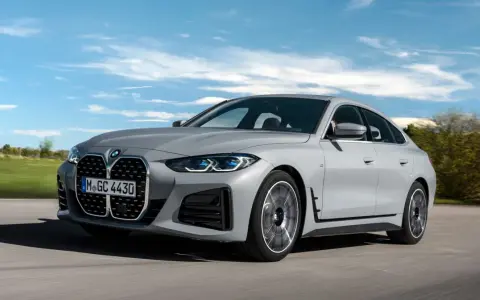 Eleganckie, szare BMW Gran Coupé sunie po drodze na tle błękitnego nieba z chmurami.