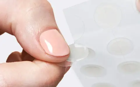 Une main retire délicatement un patch boutons d'une feuille, prêt à agir contre les imperfections.