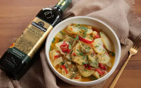 Un tazón de patatas a lo pobre, con pimientos rojos y verdes, perejil picado y una botella de aceite de oliva virgen extra.