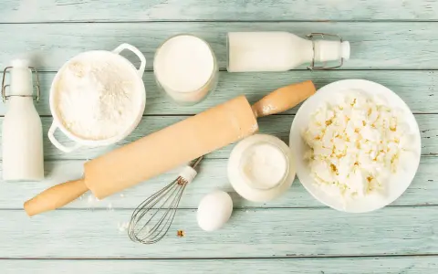 Zutaten für butter ersatz backen: Mehl, Milch, Quark, Ei, Schneebesen und Nudelholz auf blauem Holzuntergrund.