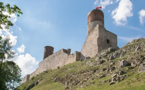 Ruiny zamku na skalistym wzgórzu w paśmie gór świętokrzyskich. Biało-czerwona flaga powiewa na wieży.