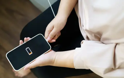 En person kopplar in sin iPhone som drar mycket batteri. Batteriikonen visar låg laddning.