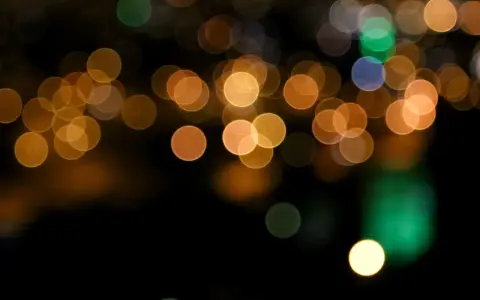 Des lumières de ville floues créent un arrière-plan bokeh chaleureux, avec des cercles dorés, verts et bleus sur fond noir.