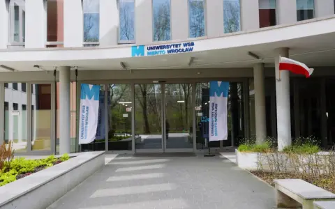 Wejście do Uniwersytetu WSB Merito Wrocław. Flagi z logo uczelni i polska flaga. Idealne miejsce na studia anglistyka Wrocław.