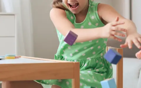 Ein Mädchen in einem grünen Kleid wirft bunte Holzklötze. Ein Versuch, laute Kinder zur Ruhe zu bringen, indem man sie zum Spielen anregt.