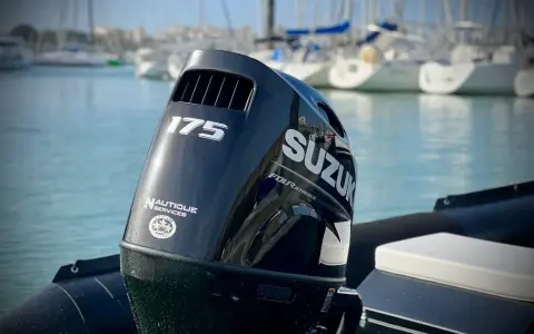 Moteur hors-bord Suzuki 175 CV, prêt pour une longue journée sur l'eau. Le mât de l'arbre est visible, avec des voiliers en arrière-plan.