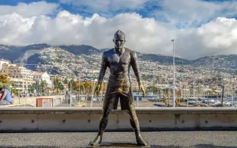 Bronzestatue von Cristiano Ronaldo am Hafen von Funchal, Madeira. Hinter ihm erstreckt sich die Stadt bis zu den Bergen. Ein Denkmal für den weltberühmten Fußballer, das man fast wie am **cristiano ronaldo flughafen** erwarten könnte.