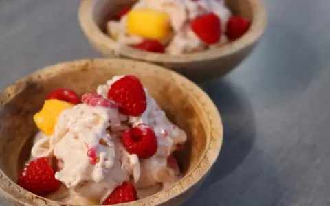 Två skålar med krämig proteinglass, toppad med hallon och mangobitar. Ett perfekt recept för en hälsosam dessert.