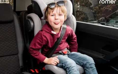 Chłopiec w foteliku samochodowym Britax Römer, zgodnym z normą ece r44/04, wyciąga język.