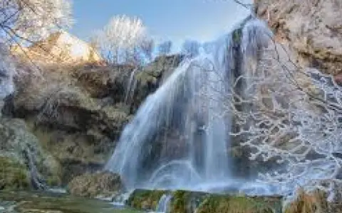 Cascada helada en el nacimiento del río Júcar, con ramas cubiertas de escarcha y agua cayendo sobre rocas.