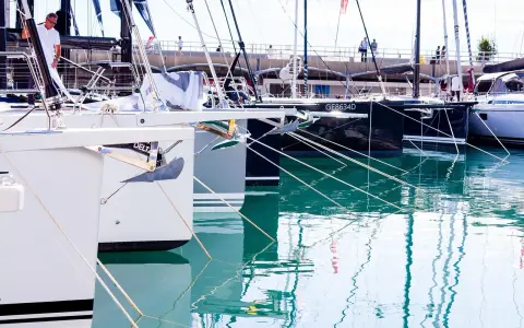 Des voiliers modernes, prêts à prendre la mer, sont amarrés dans un port. Leurs proues blanches et leurs ancres visibles rappellent le cale bateau.