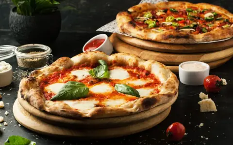 Dwie pyszne pizze, jedna margherita, druga z dodatkami. Obok sosy i pomidorki, idealne dodatki do pizzy.