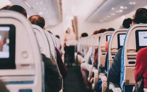 View from inside an airplane cabin, showing rows of seats with passengers and entertainment screens.
