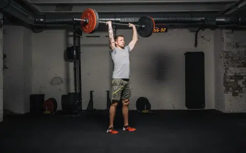 Mann führt einen **strict press** mit einer Langhantel im Fitnessstudio aus.