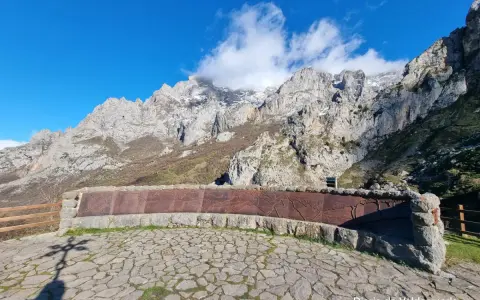 Impresionante mirador de los Picos de Europa con un muro de piedra y metal decorado. El sol ilumina las majestuosas montañas.