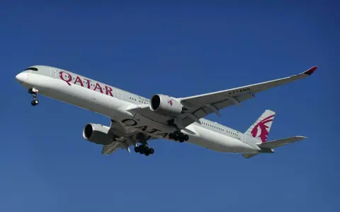 Samolot Qatar Airways z wysuniętym podwoziem, gotowy do lądowania. Idealny do podróży z bagażem podręcznym.