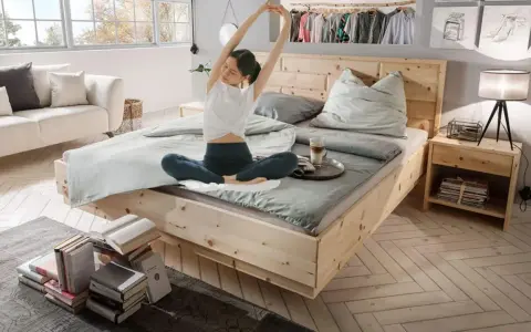 Frau dehnt sich im hellen Schlafzimmer. Ein gemütliches Bett, ein Sofa und Bücher laden zum Entspannen ein. Perfekt, um das Schlafzimmer einzurichten.
