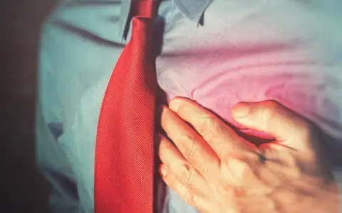 Mężczyzna w koszuli i krawacie trzyma się za klatkę piersiową, odczuwając ból. Może to być jeden z objawów niepożądanych diuretyków.