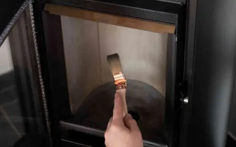 Mano con pennello per pulire il vetro della stufa bruciato.