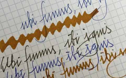 Papel cuadriculado con escritura a mano en tinta azul y marrón. Se lee "ubi fumus, ibi ignis" repetidamente.